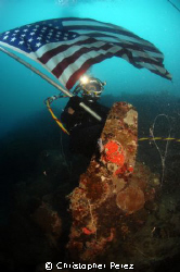 US NAVY DIVER WAVES AMERICAN FLAG OVER A WORLD WAR 2 AERI... by Christopher Perez 